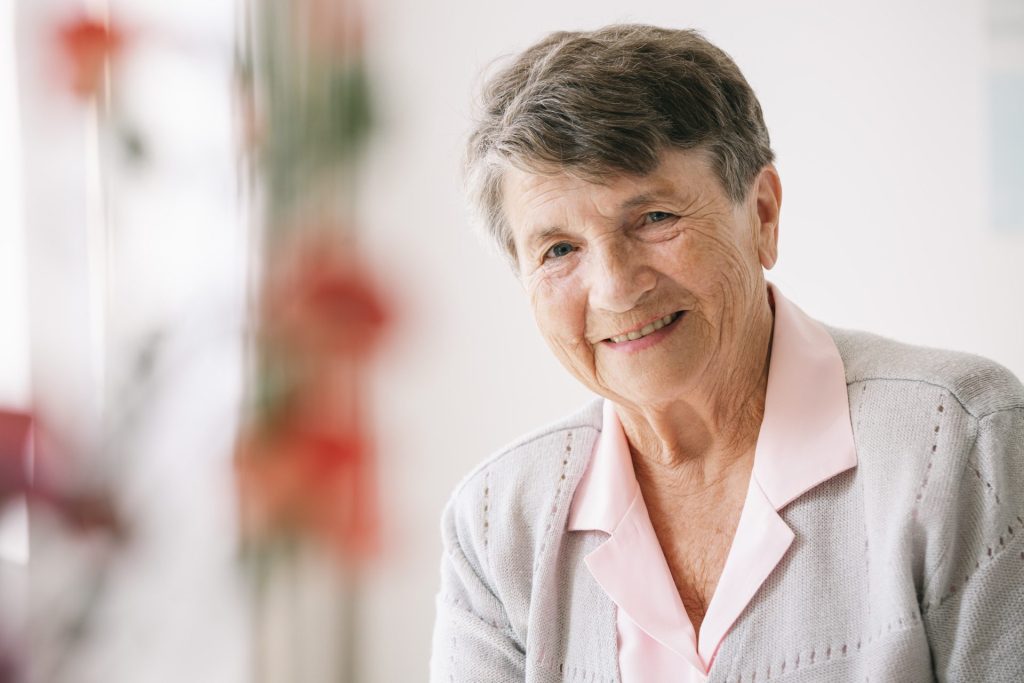 Senior woman is smiling at the camera. She is wearing a grey cardigan.