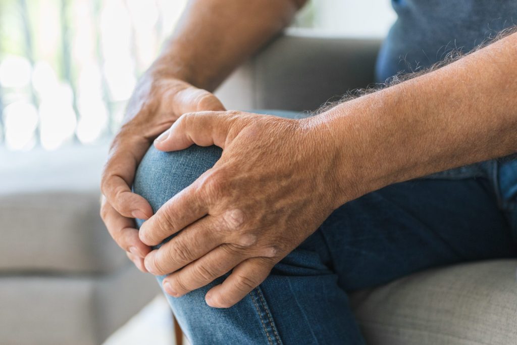 Elderly hands are holding a knee as if the knee was in pain.